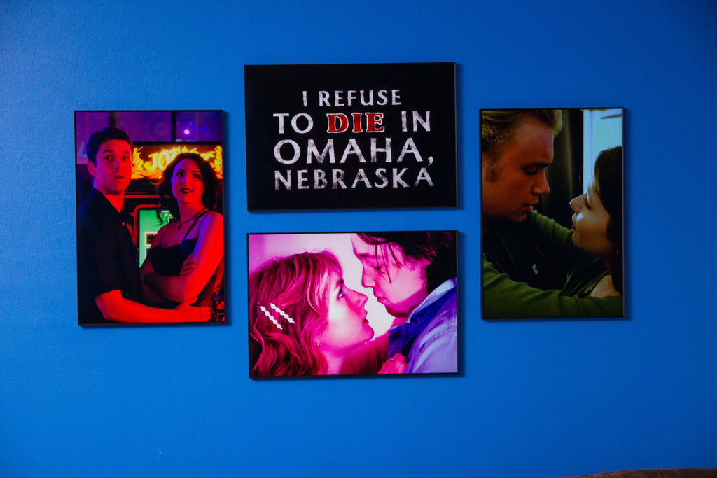 Four framed movie posters on a blue wall with 'I Refuse to Die in Omaha, Nebraska' prominently displayed.