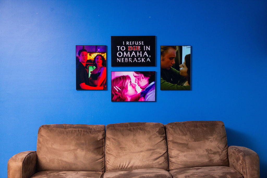 Four framed posters on a blue wall above a brown sofa.